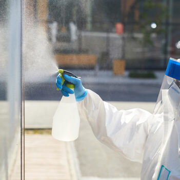 Worker Cleaning Glass Windows Outdoors Side view portrait of female worker wearing protective suit spraying chemicals over building wall during disinfection, copy space